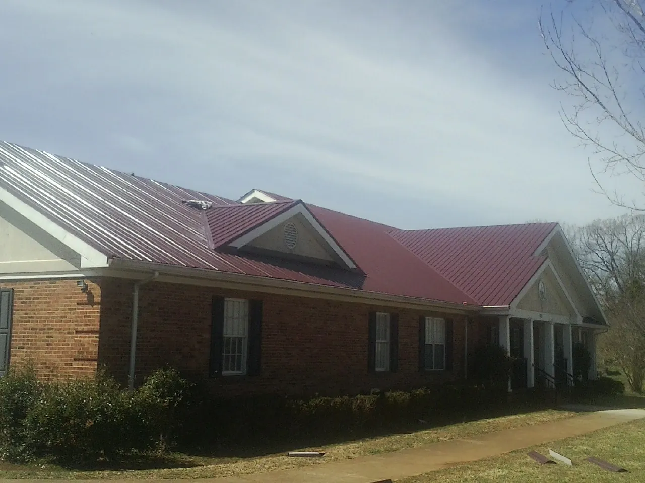 Red metal roof with gabled entries on a long brick building, from a Hail Damage Roof Repair job in Littlestown