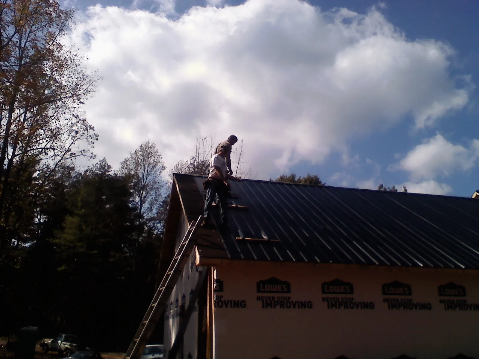 Roofer fastening dark metal panels high against a cloudy sky, from a Roof Inspection job in Littlestown