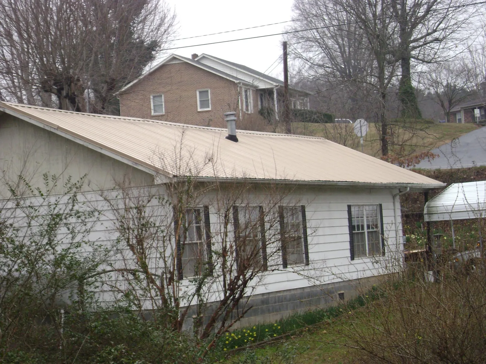 Tan metal roof on a white sided house set into a hillside — Commercial Roofing by Roofing Brothers in Littlestown